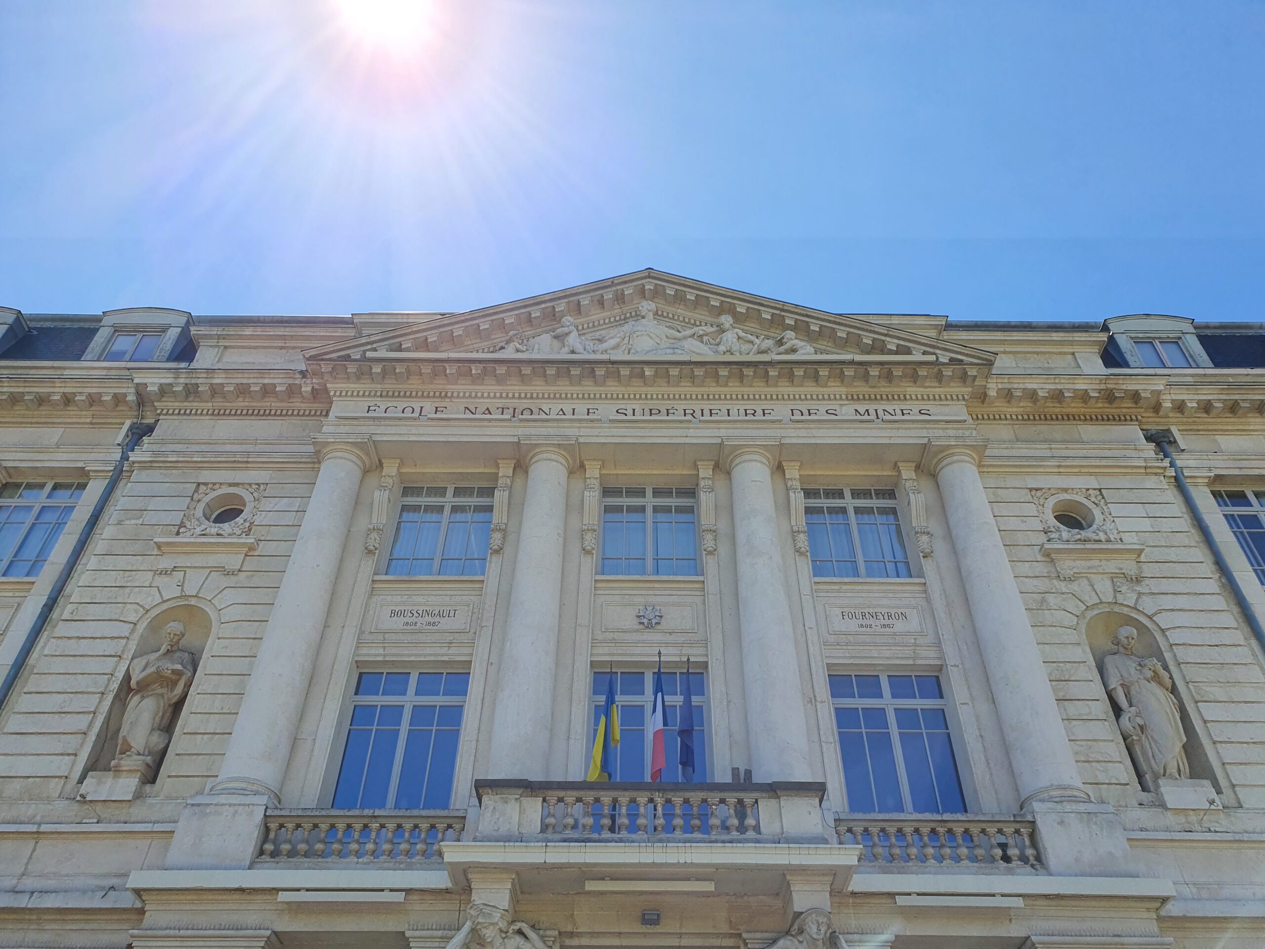 Façade of the École Nationale Supérieure des Mines de Saint-Étienne under a bright blue sunny sky.