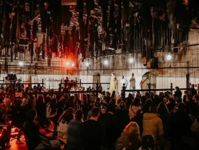 Un public nombreux assiste à un spectacle dans une grande halle industrielle éclairée de lumières rouges.