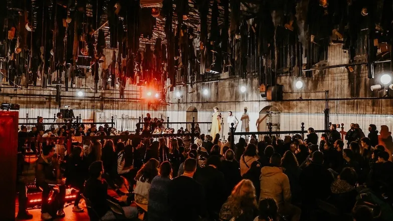 Un public nombreux assiste à un spectacle dans une grande halle industrielle éclairée de lumières rouges.
